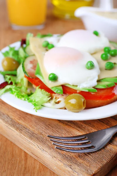 Sandwich with poached eggs, cheese and vegetables on plate on wooden background — Stock Photo, Image