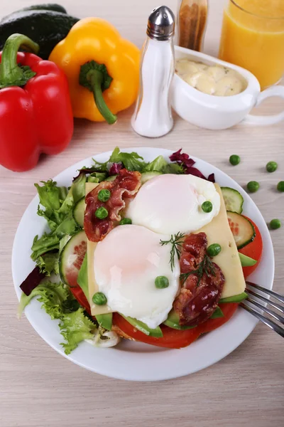 Smörgås med pocherat ägg, bacon och grönsaker på tallriken på trä bakgrund — Stockfoto