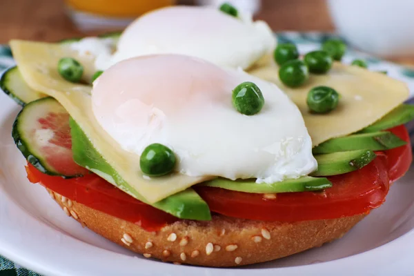 Sandwich with poached eggs, cheese and vegetables on plate on table close up — Stock Photo, Image