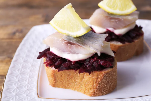 Rye toasts with herring and beets on plate on wooden background — Stock Photo, Image