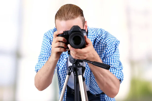 Handsome photographer with camera on tripod indoors — Stock Photo, Image