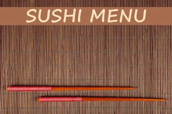 Pair of chopsticks and Sushi Menu text on brown bamboo mat background — Stock Photo, Image