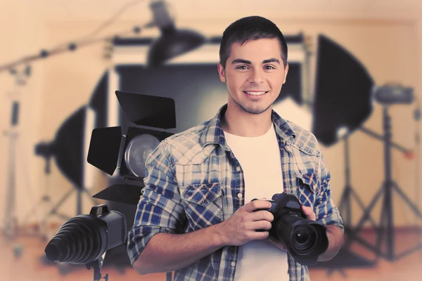 Joven fotógrafo con cámara sobre fondo de estudio fotográfico — Foto de Stock