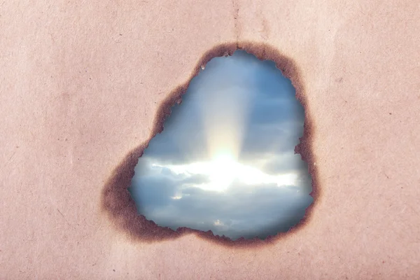 Fond bleu ciel avec des nuages à travers un trou dans du papier artisanal — Photo