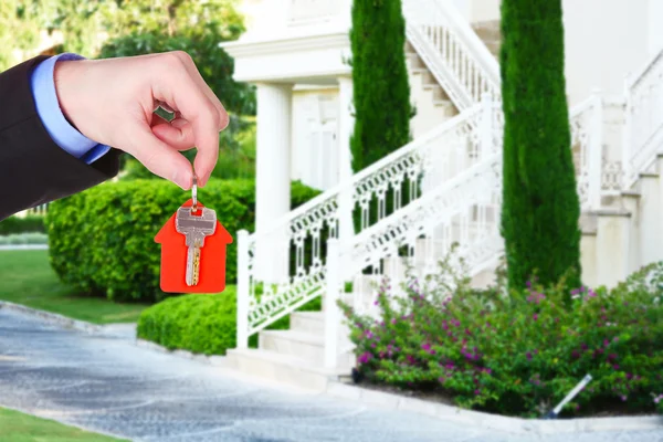 Nyckeln i handen på huset bakgrund, Real estate koncept — Stockfoto