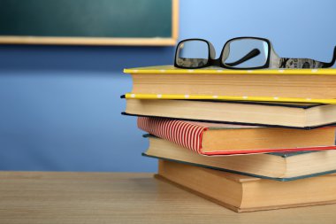 Ahşap masa, renkli duvar ve karatahta zemin üzerinde gözlüklü kitap yığını