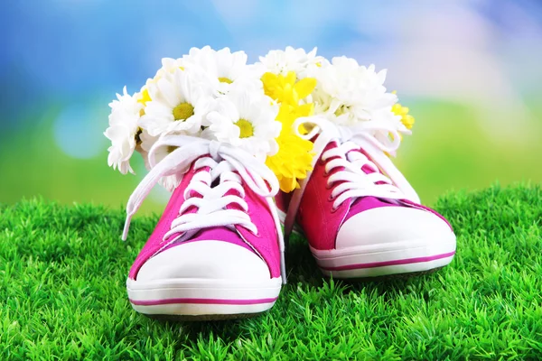 Hermosos zapatos de goma con flores en el interior sobre hierba verde, sobre fondo brillante — Foto de Stock