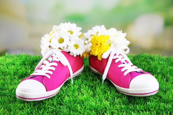 Schöne Gummischuhe mit Blumen drinnen auf grünem Gras, auf hellem Hintergrund — Stockfoto