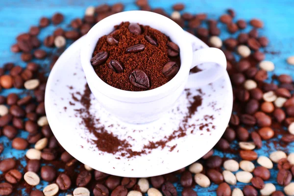 Coffee beans in white ceramic cup with saucer on blue wooden background — Stock Photo, Image