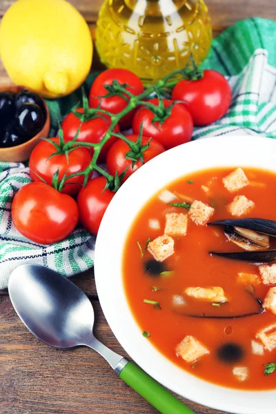 Tasty soup with mussels, tomatoes and black olives in bowl on wooden background — Stock Photo, Image