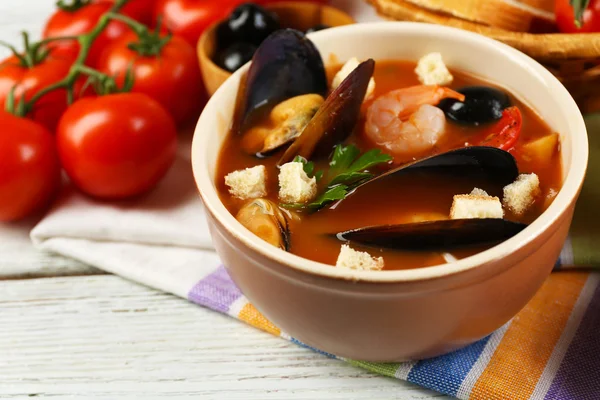 Tasty soup with shrimps, mussels, tomatoes and black olives in bowl on wooden background — Stock Photo, Image