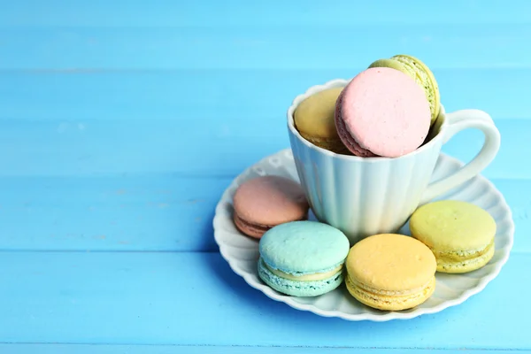 Assortment of gentle colorful macaroons in colorful mug on color wooden background — Stock Photo, Image