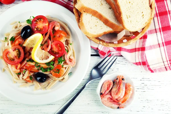 Pasta saporita con gamberetti, olive nere e salsa di pomodoro su piatto su fondo di legno — Foto Stock