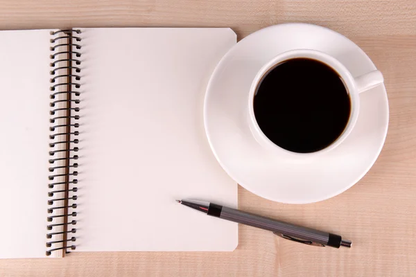 Tasse de café sur soucoupe avec cahier et stylo sur fond de table en bois — Photo