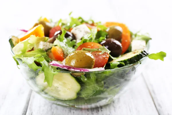 Griechischer Salat in Glasschale auf farbigem Holztischhintergrund — Stockfoto