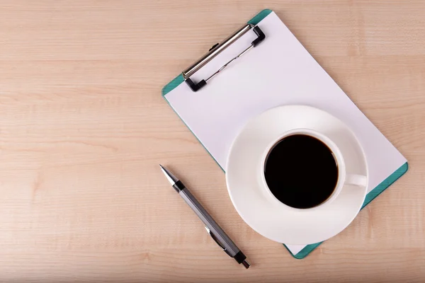 Tasse de café sur soucoupe avec feuille de papier et stylo sur fond de table en bois — Photo