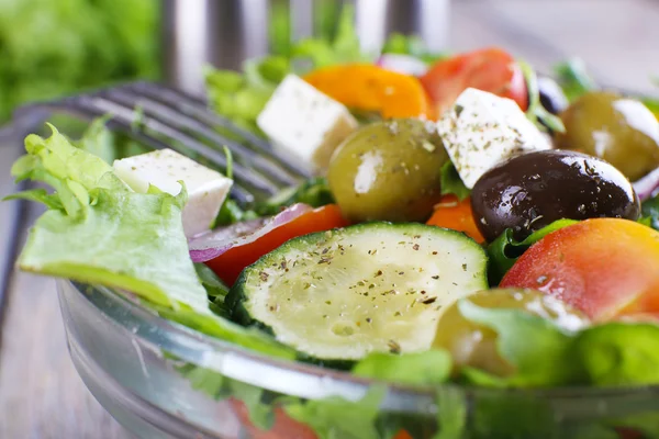 Salade grecque dans un plat en verre avec fourchette sur fond de table en bois — Photo