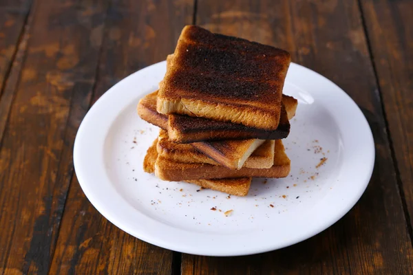 Burnt toast bread on plate, on wooden table background — Stock Photo, Image