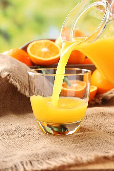 Выливание апельсинового сока из стеклянного графина, на деревянный стол и яркий фон — стоковое фото