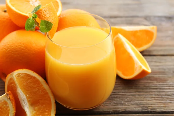 Copo de suco de laranja e fatias em fundo de mesa de madeira — Fotografia de Stock