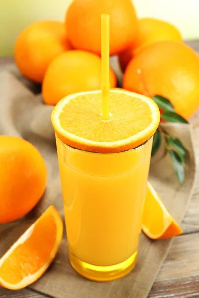 Copo de suco de laranja com palha e fatias em fundo de mesa de madeira — Fotografia de Stock