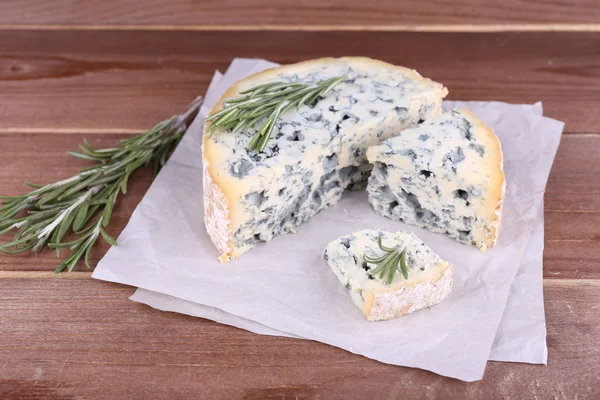 Blue cheese with sprigs of rosemary on sheets of paper and wooden table background — Stock Photo, Image