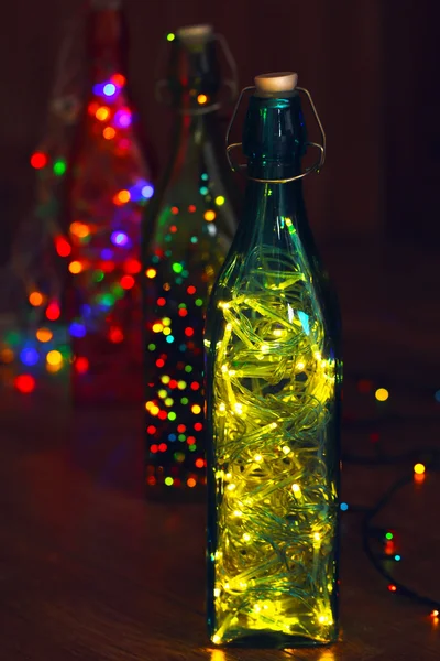 Christmas lights in bottles on wooden background — Stock Photo, Image