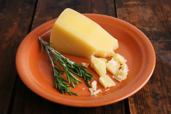 Parmesan cheese with sprig of rosemary on plate on wooden table background — Stock Photo, Image