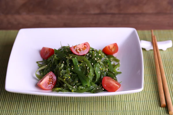 Seaweed salad with slices of cherry tomato on bamboo mat and wooden table background — Stock Photo, Image