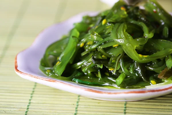 Insalata di alghe in piatto su sfondo tappetino di bambù — Foto Stock