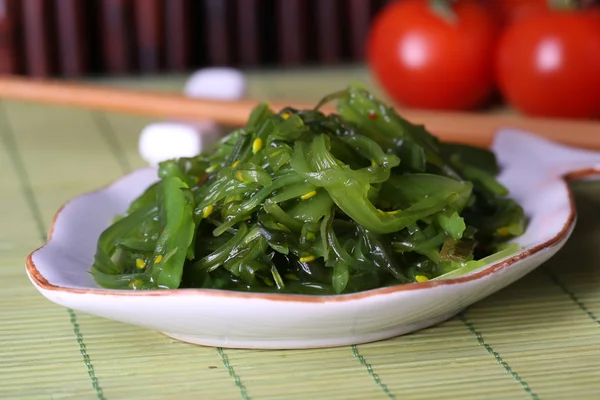 Ensalada de algas en plato con bambú sobre fondo — Foto de Stock