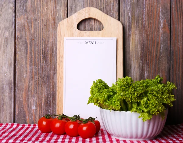 Cutting board with menu sheet of paper, with cherry tomatoes and lettuce on wooden planks background — Stock Photo, Image