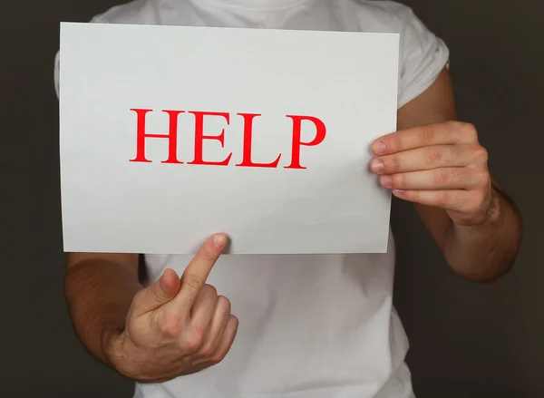 Sheet of paper with Help sign in male hands on dark background — Stock Photo, Image