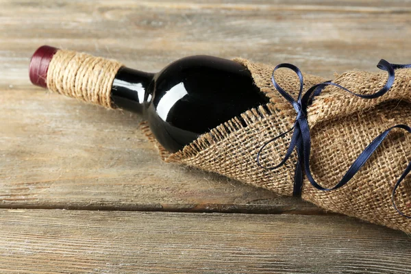 Red wine bottle wrapped in burlap cloth on wooden planks background — Stock Photo, Image