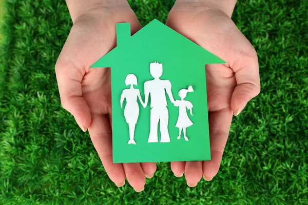 Cutout house with paper family in female hands on green grass background — Stock Photo, Image