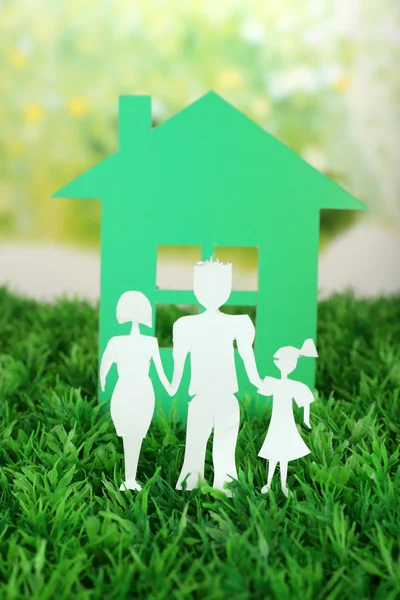 Découpage famille de papier et maison sur herbe verte et fond flou lumineux — Photo