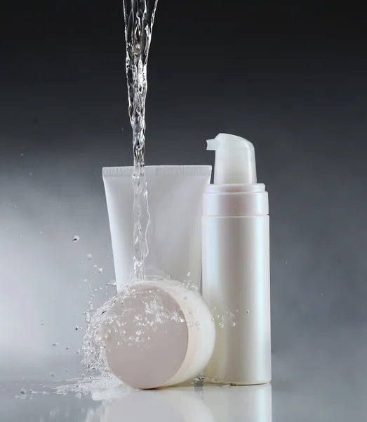 Cosmetic products in water splashes on gray background — Stock Photo, Image