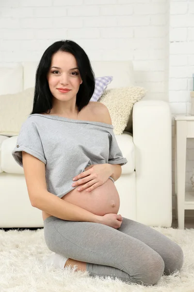 年轻孕妇坐在地毯上家庭室内背景 — 图库照片