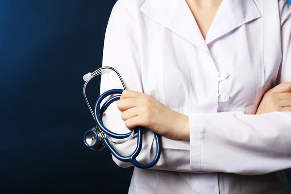 Primer plano de la mano del médico con estetoscopio sobre fondo azul oscuro — Foto de Stock