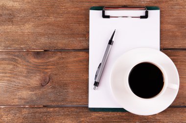 Fincan kahve fincan tabağı üzerinde kağıt ve kalem ahşap masa arka plan üzerinde levha ile