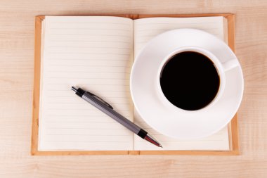 Fincan kahve üzerinde uçan daire ile açık defter ve kalem ahşap masa arka plan üzerinde