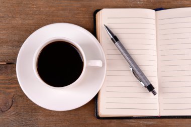 Fincan kahve tabağı ile günlüğü üzerinde ve ahşap masa arka plan üzerinde kalem