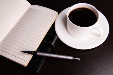 Fincan kahve tabağı ile günlüğü üzerinde ve ahşap masa arka plan üzerinde kalem