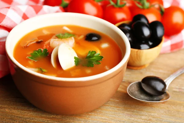 Tasty soup with shrimps, mussels, tomatoes and black olives in bowl on wooden background — Stock Photo, Image