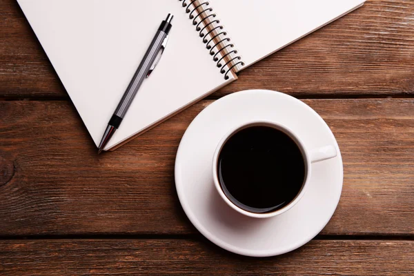 Tazza di caffè su piattino con taccuino e penna su sfondo tavolo in legno — Foto Stock