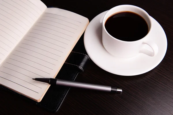 Tasse Kaffee auf Untertasse mit Tagebuch und Stift auf Holztischhintergrund — Stockfoto