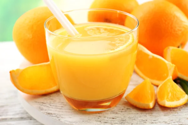 Copo de suco de laranja com palha e fatias em fundo de mesa de madeira — Fotografia de Stock