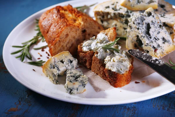 Blue cheese with sprigs of rosemary, bread and nuts on plate and color wooden table background — Stock Photo, Image