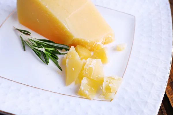 Parmesan cheese with sprig of rosemary on plate on wooden table background — Stock Photo, Image