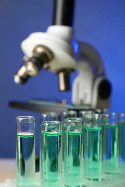 Микроскоп и пробирки на столе, на цветном фоне — стоковое фото